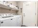 Bright laundry room featuring a washer and dryer, storage shelf and a door with coat hooks at 44976 W Miramar Rd, Maricopa, AZ 85139