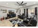 Living room featuring black leather seating, a large TV, a modern ceiling fan, and decor at 25947 W Oraibi Dr, Buckeye, AZ 85396