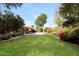 Spacious backyard with lush green grass, mature trees, colorful flowers, and covered patio at 6126 W Paradise Ln, Glendale, AZ 85306