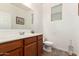 Bright bathroom features a wood vanity, white sink, large mirror, toilet, and a window with blinds at 2324 W Melody Dr, Phoenix, AZ 85041