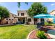 Expansive backyard featuring lush green grass, mature trees, covered patio, and an outdoor seating area with an umbrella at 13005 W Vista Paseo Dr, Litchfield Park, AZ 85340