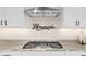 Detailed view of a modern gas cooktop with a stainless steel vent hood and white cabinetry at 23010 E Pummelos Rd, Queen Creek, AZ 85142