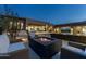 Luxurious backyard with a fire pit, ample seating, a pool, outdoor dining, and desert landscaping at dusk at 9456 E Sands Dr, Scottsdale, AZ 85255