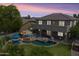A luxurious backyard at dusk featuring a pool, fire pit, lounge chairs, and an outdoor cooking area under the patio at 35952 W Catalonia Dr, Maricopa, AZ 85138