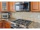 Modern kitchen featuring a stainless steel gas range, granite counters, tiled backsplash, and wooden cabinetry at 35952 W Catalonia Dr, Maricopa, AZ 85138