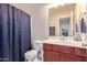 Cozy bathroom featuring a vanity with cherry wood cabinets, framed mirror, and a shower-tub combination with a blue curtain at 25447 W Heathermoor Dr, Buckeye, AZ 85326