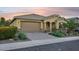 Home featuring a well manicured yard with desert landscaping, a large garage, and a covered porch with warm lighting at 19002 N Arbor Dr, Maricopa, AZ 85138