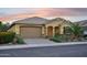Home featuring a well manicured yard with desert landscaping, a large garage, and a covered porch with warm toned lighting at 19002 N Arbor Dr, Maricopa, AZ 85138