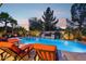 Beautiful backyard pool with lounge chairs, water feature, and lush landscaping under a colorful twilight sky at 19002 N Arbor Dr, Maricopa, AZ 85138