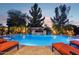 Backyard pool with illuminated water feature and lounge chairs, framed by lush landscaping under a dusk sky at 19002 N Arbor Dr, Maricopa, AZ 85138