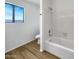 Bright bathroom featuring a shower-tub combo, toilet and wood-look floors, complemented by a window view at 8831 N 63Rd Dr, Glendale, AZ 85302