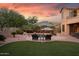 A backyard oasis features a stunning pool, lounge chairs, and meticulous landscaping against a vibrant sunset at 18432 W Port Royale Ln, Surprise, AZ 85388
