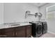 Bright laundry room featuring a sink, granite counters, storage shelves, and modern black Samsung washer and dryer at 18493 W Hiddenview Dr, Goodyear, AZ 85338