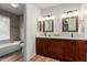 Well-lit bathroom with double sinks, granite countertops, wood cabinets, and a tiled shower/bath combination at 19 W Wickieup Ln, Phoenix, AZ 85027