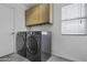 Well-lit laundry room includes a side-by-side washer and dryer, upper cabinets and a window at 4530 E Desert Wind Dr, Phoenix, AZ 85044