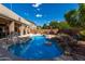 Landscaped backyard showcasing a swimming pool with rock features, a covered patio, and mature trees at 4321 E Morenci Rd, San Tan Valley, AZ 85143