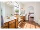 Bright bathroom featuring double vanity sinks, an arched window, wood-look floors, and an arched doorway to the bedroom at 8977 E Ludlow Dr, Scottsdale, AZ 85260