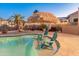 Beautiful backyard pool with a tiki umbrella and seating, surrounded by lush landscaping and decorative lighting at 16375 W Cortez St, Surprise, AZ 85388