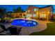 A beautifully illuminated backyard featuring a sparkling pool, comfortable lounge chairs, and a charming home with warm lighting at 24433 N 75Th St, Scottsdale, AZ 85255