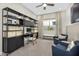 Well-lit home office with custom shelving, desk, comfortable chairs, and large window at 14825 W Whitehorn Way, Surprise, AZ 85387