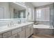 Bright bathroom features a large, illuminated mirror, double sinks, and a luxurious soaking tub with window shutters at 10490 E Morning Star Dr, Scottsdale, AZ 85255
