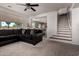 Bright living room featuring a dark sectional sofa, carpet flooring, and stairway leading to the upper level at 17413 W Mandalay Ln, Surprise, AZ 85388