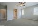 Bright carpeted bedroom features a ceiling fan and two windows with an ensuite bathroom and walk-in closet at 41279 W Elm Dr, Maricopa, AZ 85138