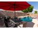 Inviting pool with rock waterfall and tiki decor complemented by outdoor dining area under a red umbrella at 7826 W Mcrae Way, Glendale, AZ 85308