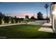 Backyard with lush lawn, in-ground pool, privacy landscaping, and evening sky at 8403 E Fairmount Ave, Scottsdale, AZ 85251