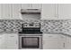 Close-up of the kitchen's stainless steel oven, mosaic tile backsplash, and white cabinets at 8750 W Granada Rd, Phoenix, AZ 85037