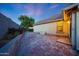 Paver patio with lush garden adjacent to a neutral colored stucco home and block wall fence at dusk at 13295 N 153Rd Ln, Surprise, AZ 85379