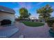 Well-maintained backyard with green lawn, gravel landscaping, stepping stones, and mature trees beneath a blue and pink sky at 13295 N 153Rd Ln, Surprise, AZ 85379