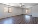 Spacious living room with hardwood floors, a ceiling fan, and natural light from two windows at 37053 W Amalfi Ave, Maricopa, AZ 85138