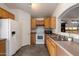 Efficient kitchen with wood cabinets, white appliances, gray tile flooring, and an open serving bar at 12410 W Flores Dr, El Mirage, AZ 85335