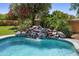 A rock waterfall spills into a gorgeous backyard pool surrounded by lush landscaping and a brick perimeter wall at 3357 N Ashbrook E St, Mesa, AZ 85213
