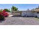 Gravel backyard featuring a covered patio, colorful bougainvillea, and a wall-mounted air conditioning unit at 4116 W Marshall Ave, Phoenix, AZ 85019