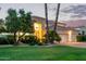 Elegant home at dusk featuring lush landscaping, mature trees, and a three car garage at 7376 E Via Estrella Ave, Scottsdale, AZ 85258