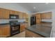 Modern kitchen with tile flooring, wooden cabinets, black appliances and granite countertops at 15905 W Saguaro Ln, Surprise, AZ 85374