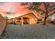 Gravel backyard featuring large tree, metal fence, and covered patio with furniture at sunset at 6520 E Hacienda La Noria Ln, Gold Canyon, AZ 85118