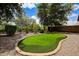 An ample backyard showcasing a well-maintained artificial putting green surrounded by gravel and mature trees at 12775 W Lowden Rd, Peoria, AZ 85383