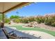 A serene backyard showcases a charming waterfall, colorful landscaping, and a covered patio for relaxation at 15658 W Arbor Trl, Surprise, AZ 85374