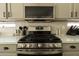 Close up on a stainless steel gas range in the kitchen with tile backsplash and gray cabinets at 4064 E Reins Rd, Gilbert, AZ 85297