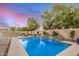 Backyard pool with waterfalls, desert landscaping, hardscape and trees at dusk at 4453 S Huachuca Way, Chandler, AZ 85249