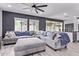 Spacious living room featuring a gray sectional sofa, wooden floors, large windows, and modern ceiling fan at 1914 N Marketside Ave, Buckeye, AZ 85396
