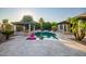 Inviting backyard pool area with lush landscaping, a covered patio, fire features, and travertine tile at 15803 W Almeria Rd, Goodyear, AZ 85395