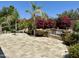 The backyard features a stone-paved patio and lush landscaping with mature trees, a water feature, and vibrant flower beds at 562 E Vesper Trl, Queen Creek, AZ 85140