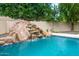Inviting pool with rock waterfall slide, lush landscaping, and clear blue water at 8219 S Pecan Grove Cir, Tempe, AZ 85284
