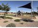 Community playground featuring covered seating areas, play structures, and desert landscaping under a blue sky at 40060 W Wade Dr, Maricopa, AZ 85138