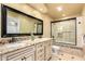 Bright bathroom with a double sink vanity with a black countertop, a shower with glass doors at 7722 W Libby St, Glendale, AZ 85308
