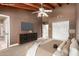 Virtually staged main bedroom featuring a wooden beamed ceiling, neutral paint and a large tv at 7722 W Libby St, Glendale, AZ 85308